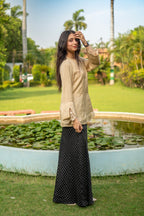 Woman in beige top and black polka dot skirt standing in a garden with a pond and greenery.