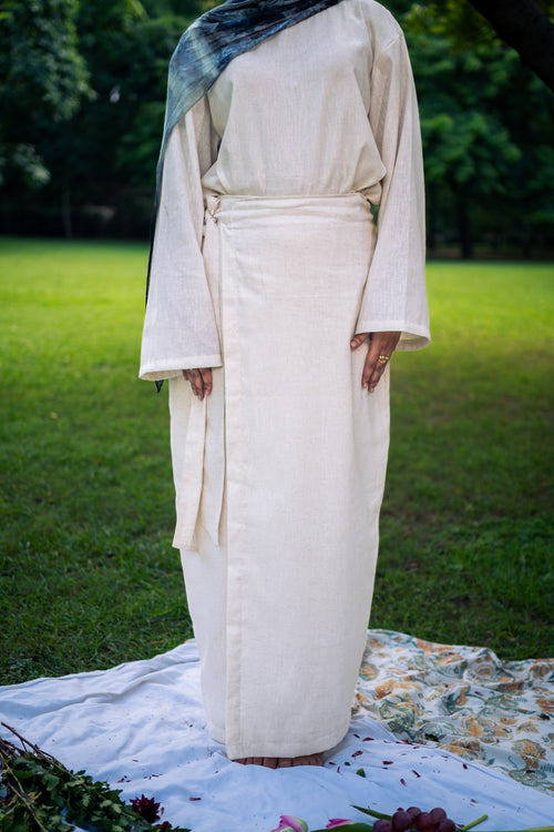 Person wearing a long, light-colored dress standing on grass with a floral blanket.