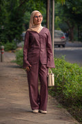 Woman in a maroon striped outfit walking on a sidewalk with greenery and a road in the background.