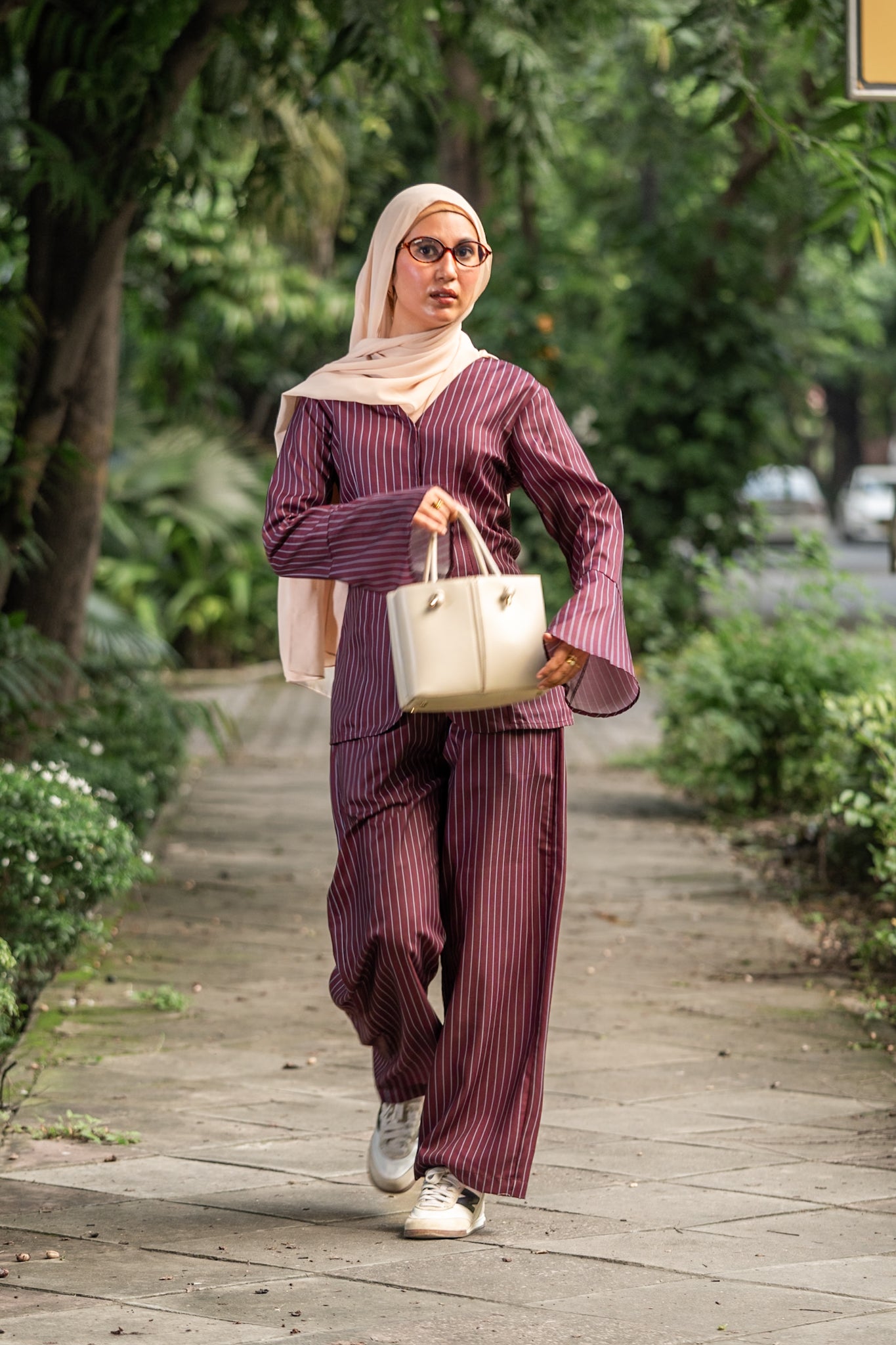 Woman in a striped outfit walking outdoors on a wooden path with greenery.