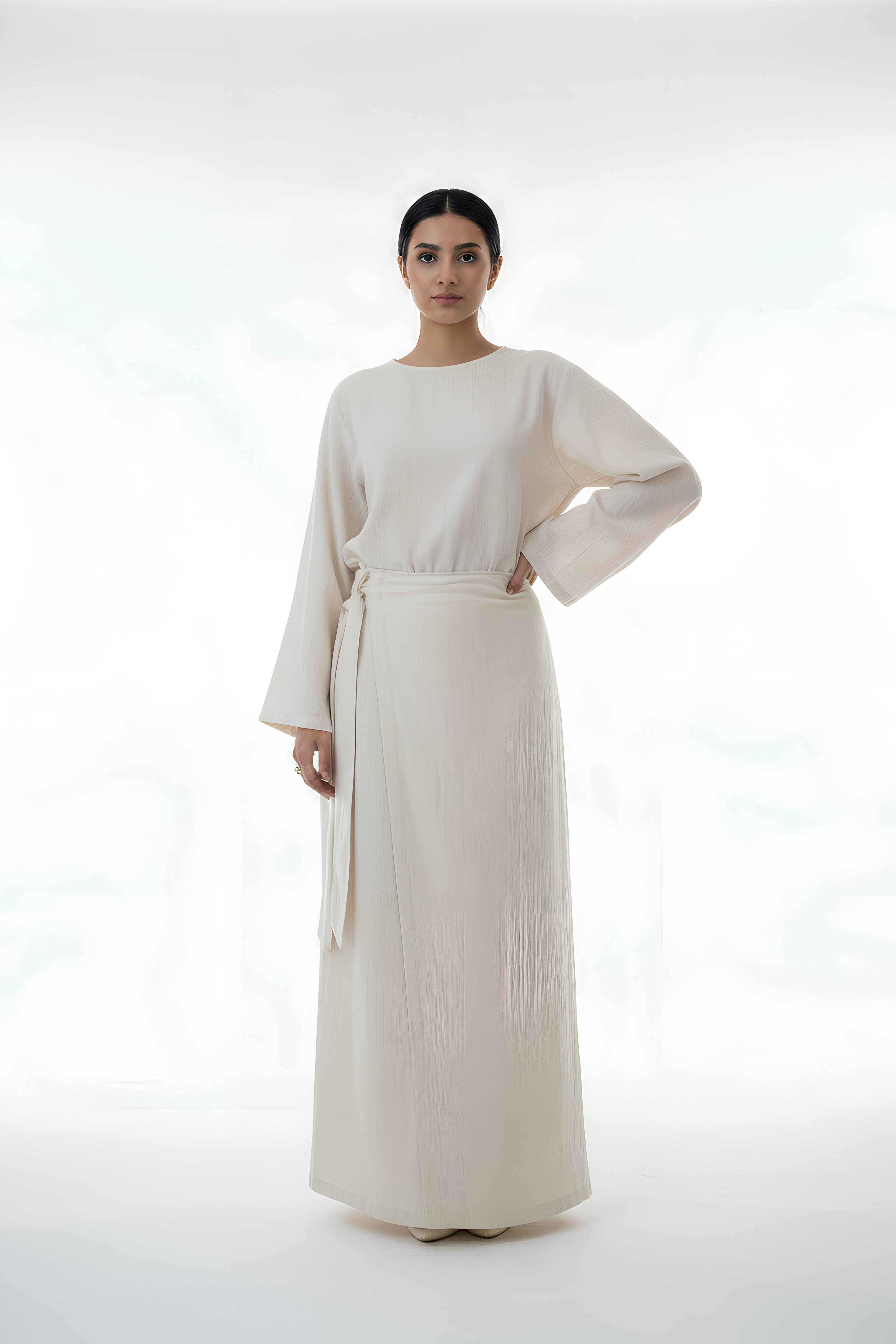 Woman wearing a long, light-colored dress with a belt on a white background